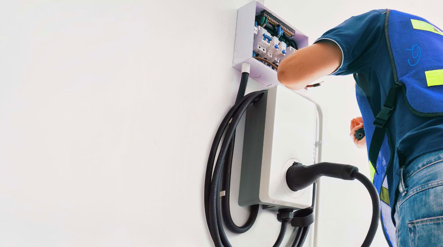 Borne de recharge pour véhicule électrique fixée sur la façade d'une maison contemporaine avec câble rangé dans un environnement extérieur lumineux